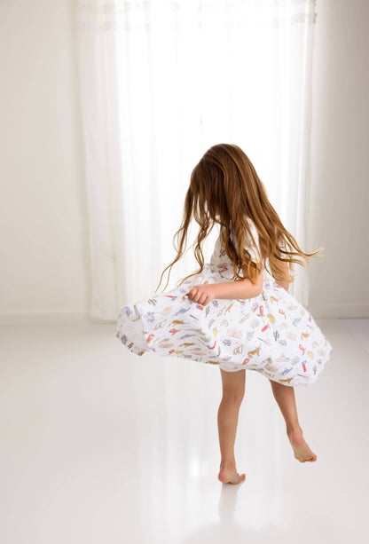 Young girl in a white dress with colorful Texas patterns standing in a bright room.