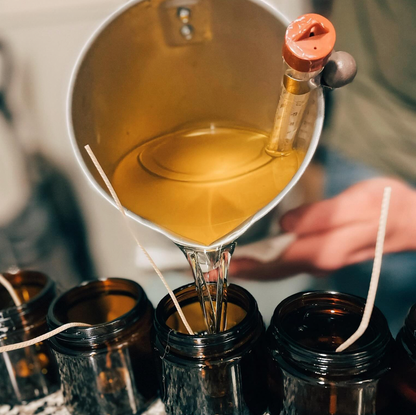 Person pouring a candles into small jars using a funnel.