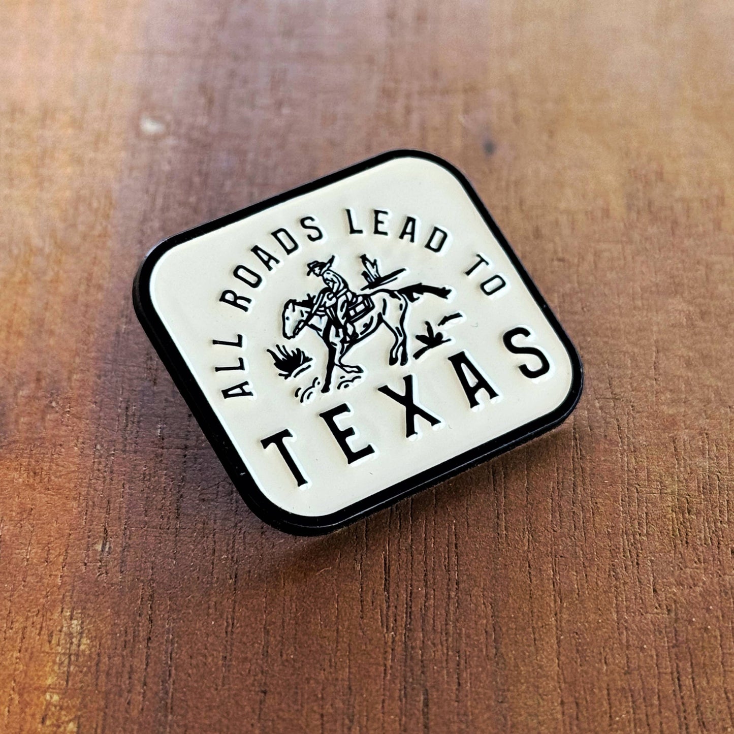 Pin with 'All Roads Lead to Texas' text on a wooden surface