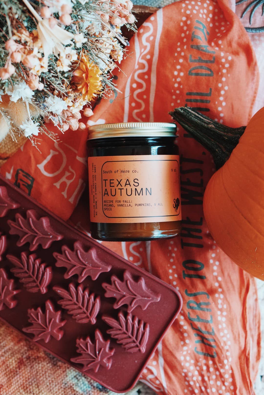 Jar of 'Texas Autumn' candle with decorative elements on a textured surface