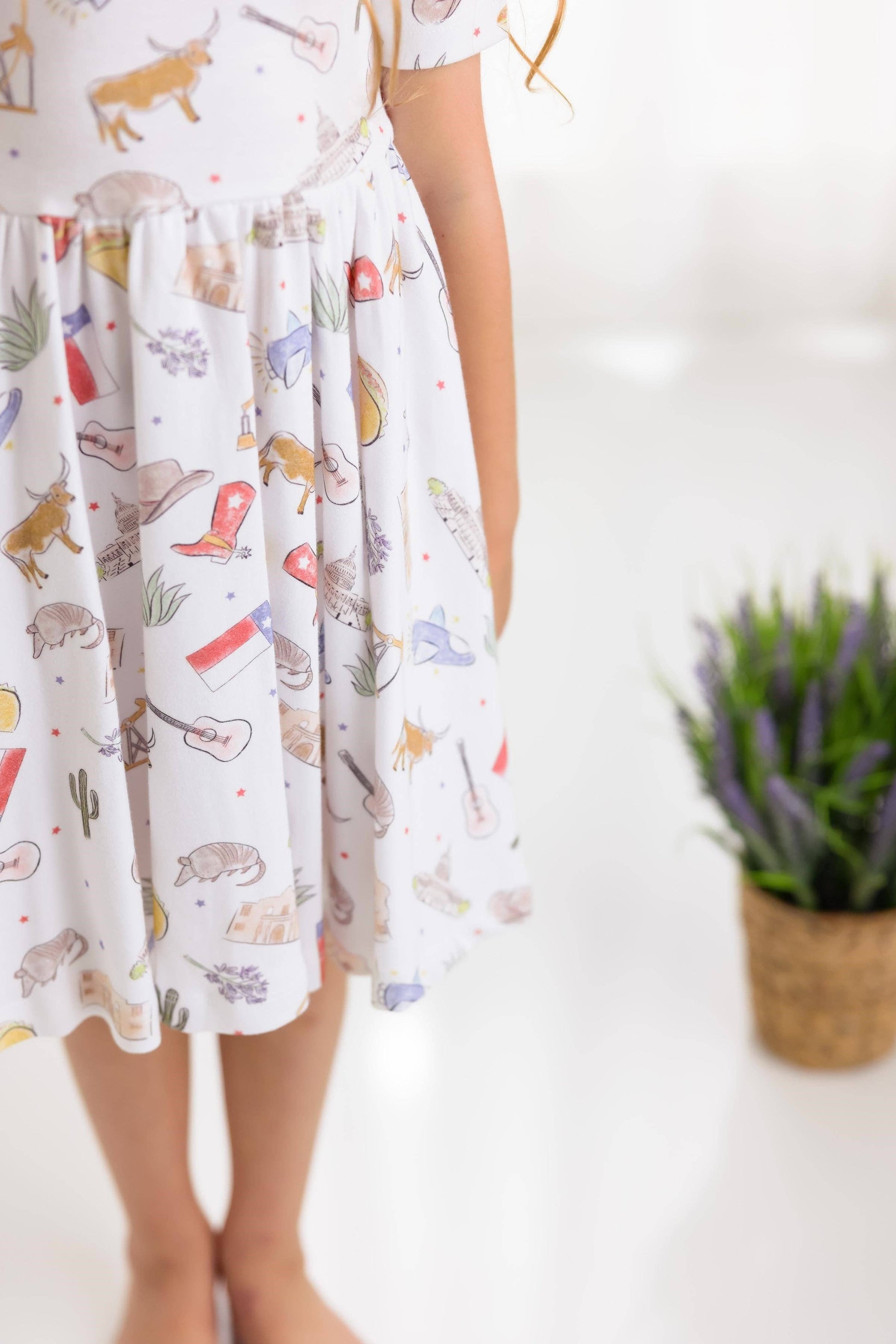 Girl wearing a dress with Texas themed prints on a white background, longhorn, cowboy boots, Texas flag