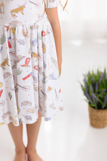 Girl wearing a dress with Texas themed prints on a white background, longhorn, cowboy boots, Texas flag