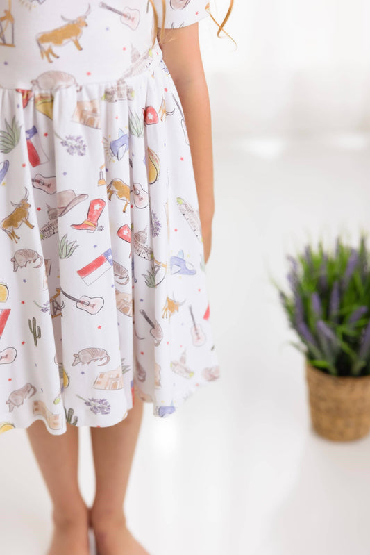 Girl wearing a dress with Texas themed prints on a white background, longhorn, cowboy boots, Texas flag